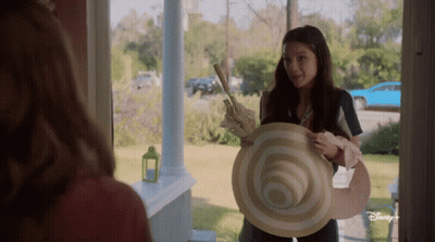 Girl Holding Large Hat In Front Of Disney Plus Door GIF