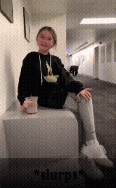 Girl In Black Hoodie Sitting On Cube Holding Coffee GIF