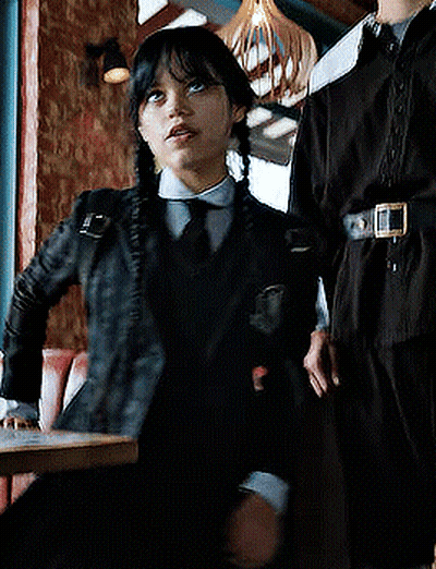 Girl In Black Jacket And Tie Sitting At Table GIF