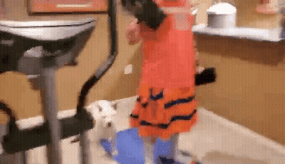 Girl In Orange Dress Standing By Dog On Exercise Bike GIF