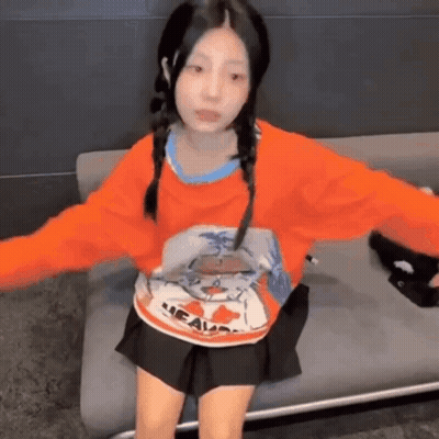 Girl in Orange Sweater and Black Skirt Sitting on Couch With Arms Outstretched