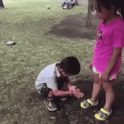 Girl In Pink Shirt Standing Beside Kneeling Boy GIF