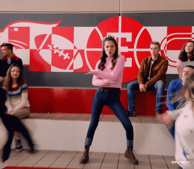 Girl In Pink Sweater Dancing In Front Of Football Wall GIF