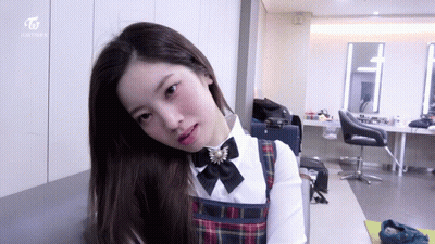 Girl In Plaid Dress Sitting In Room With Twice On Wall GIF