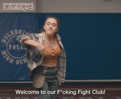 Girl In Plaid Shirt Next To Bottoms Sign GIF