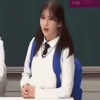 Girl In School Uniform Sitting At Desk With Blue Backpack GIF