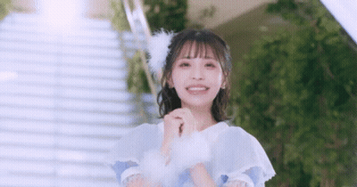Girl In White Dress With Feathers In Hair Standing In Front Of Stairs GIF