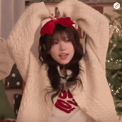 Girl In White Sweater And Red Bow In Front Of Christmas Tree GIF