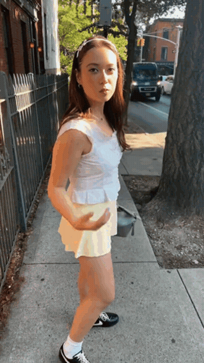 Girl In White Top And Yellow Shorts On Sidewalk GIF