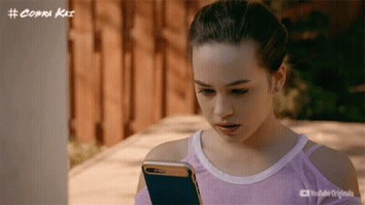 Girl Looking At Cell Phone With Cobra Kai Logo GIF