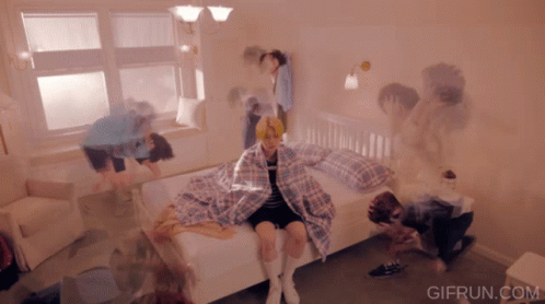 Girl Sitting On Bed Surrounded By People GIF