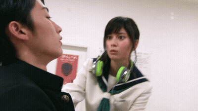 Girl With Green Headphones Talks To Boy In Front Of Sign Saying A GIF