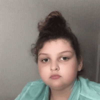Girl With Hair Bun In Green Shirt Looking At Camera GIF