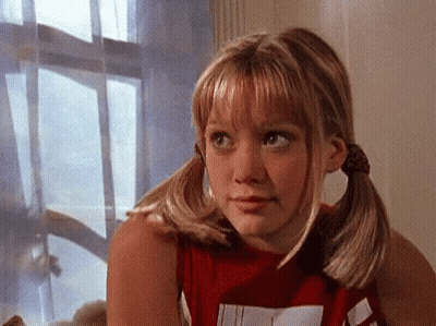 Girl With Pigtails Sitting By Window Looking At Camera GIF