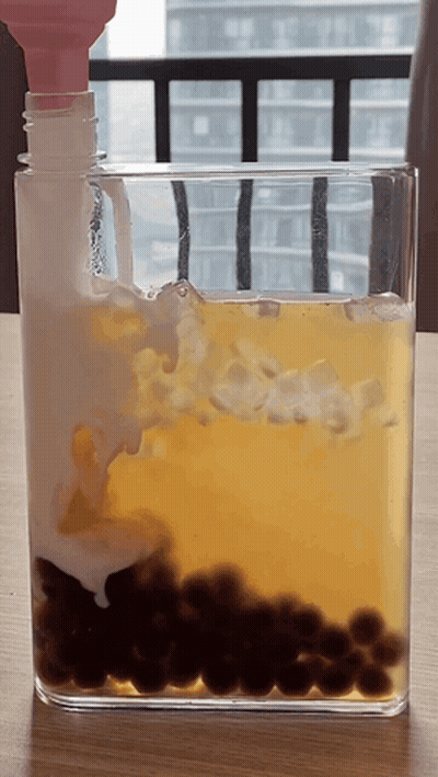 Glass Container With Yellow Liquid And Black Balls GIF