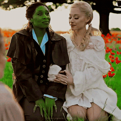 Green And Blonde Women In Costumes Sitting In Flowers GIF