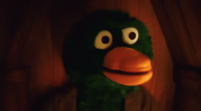 Green And Orange Stuffed Animal With Big Eyes And Beak In Dark Room GIF