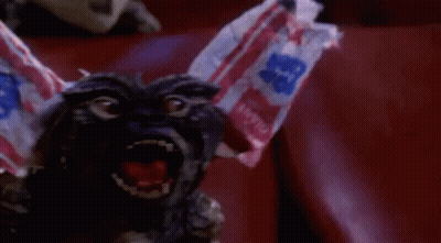 Gremlin Sitting In Red Chair With Candy Bag On Head GIF
