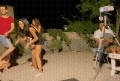 Group Dancing In Front Of Projector While Man Sits In Chair GIF
