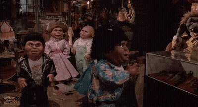 Group Of Dolls Standing In Room With Display Case GIF