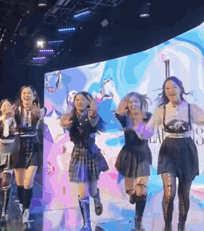 Group Of Girls Dancing On Stage With Screen Saying A GIF
