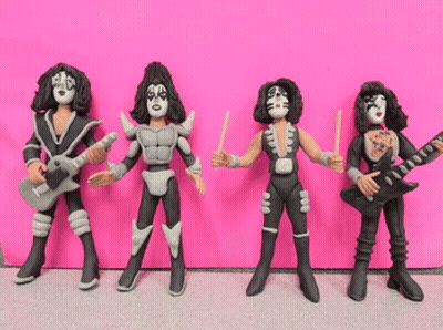 Group Of Kiss Figurines Lined Up Against Pink GIF