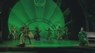 Group Of People Dancing On Stage In Front Of Clock GIF