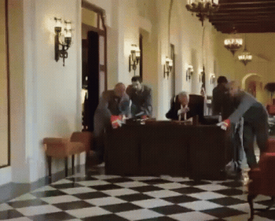 Group Of People Standing Around Table In Hallway With Checkered Floor GIF