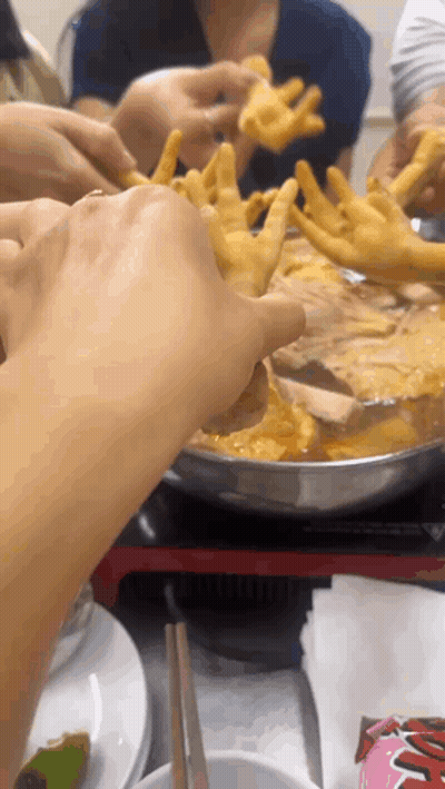 Group Reaching For Chicken Feet In Pot GIF