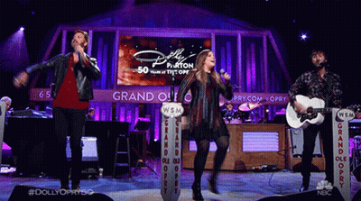 Group Singing And Playing Guitars Behind Dolly Parton Screen GIF