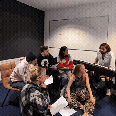 Group Sitting Around Piano With EC Sign GIF