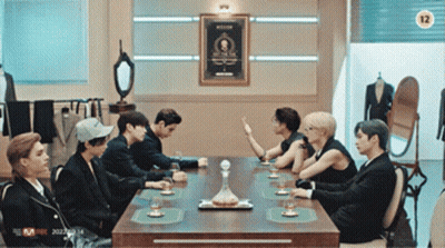 Group Sitting Around Table With Sign Saying 12 GIF