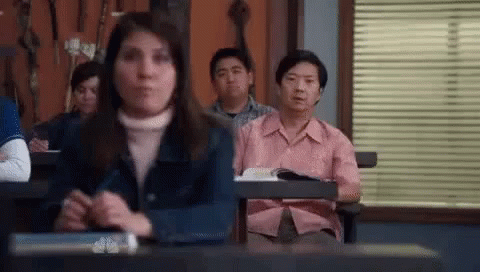 Group Sitting At Desks With Man In Pink Shirt GIF