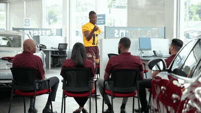 Group Sitting In Car Showroom With Man In Yellow Shirt Number 9 GIF