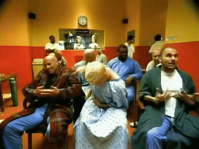 Group Sitting In Waiting Room With Clock At 12:15 GIF