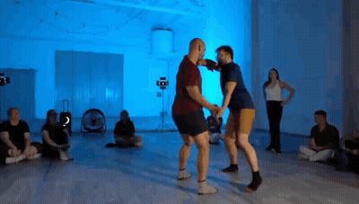 Group Sitting On Floor With Blue Lights While Two Men Dance GIF