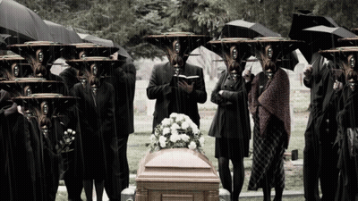 Group Standing Around Coffin In Cemetery With Umbrellas GIF