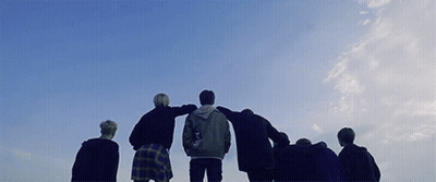 Group Standing In Circle With Arms Around Each Other Against Blue Sky GIF