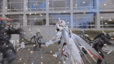 Group Standing In Front Of Building, One In White Cape GIF