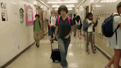 Group Walking Down School Hallway With Woman Pulling Suitcase GIF
