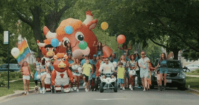 Group Walking Down Street With Balloons And Bull Mascot GIF