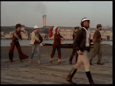Group Walking Down Street With Man In Helmet GIF