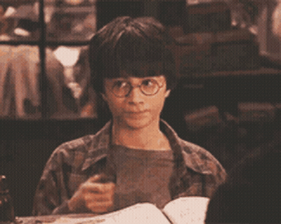 Harry Potter Is Holding A Wand While Sitting At A Table With A Book GIF