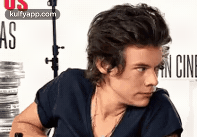 Harry Styles In Black Shirt Sitting By Film Stack GIF