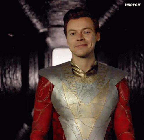 Harry Styles Is Wearing A Superhero Costume And Smiling In A Dark Hallway . GIF