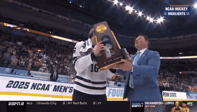 Hockey Player Holding Trophy In Front Of 2025 NCAA Men's Banner GIF