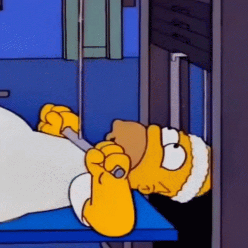 Homer Simpson Is Laying In A Hospital Bed With A Needle In His Mouth . GIF