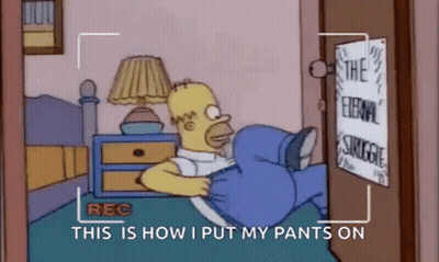 Homer Simpson Is Laying On A Bed With His Pants On And A Camera Recording Him . GIF