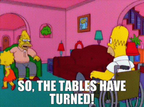 Homer Simpson Is Sitting In A Wheelchair In A Living Room Talking To A Woman . GIF