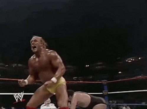 Hulk Hogan Is Standing In A Wrestling Ring With His Arms In The Air . GIF